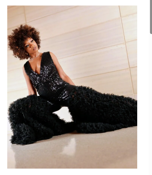 Model with curly hair seated in the black sequin ruffle bell bottom jumpsuit